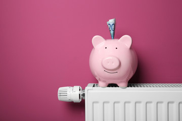 Savings concept. Piggy bank and money on heating radiator with temperature regulator on pink background