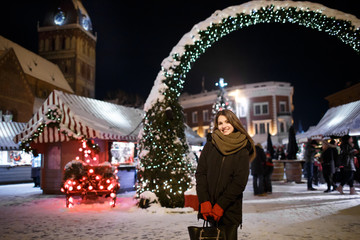 Fototapeta premium Long hair girl on European Christmas Market. Young woman Enjoying Winter Holiday Season. Blurred Lights background, dusk. Cups with drink in hand. Selective focus