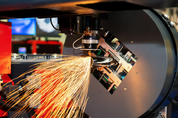 CNC laser cutting metal pipe with bright sparkle in factory.