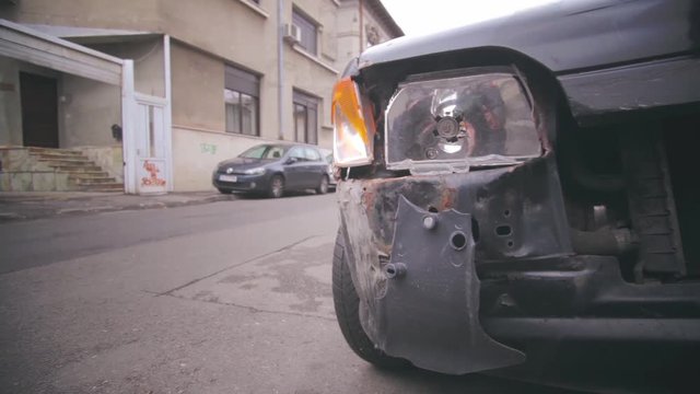 Color footage of a crashed car with broken headlight and traffic.