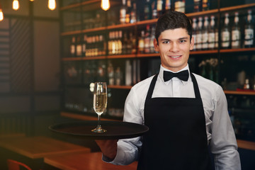 Male waiter holding tray with champagne in cafe