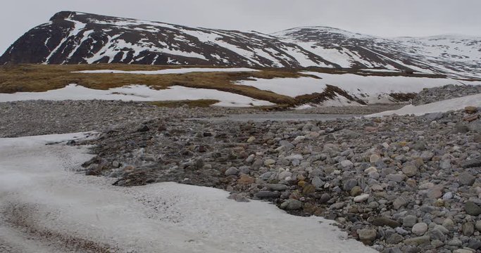 Scenic wide of arctic stream flowing under snow field in tundra