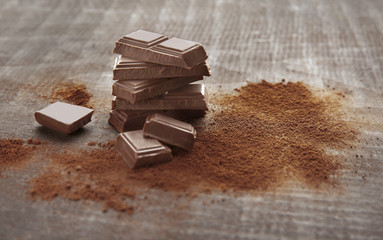 Broken chocolate pieces and cocoa powder on wooden background