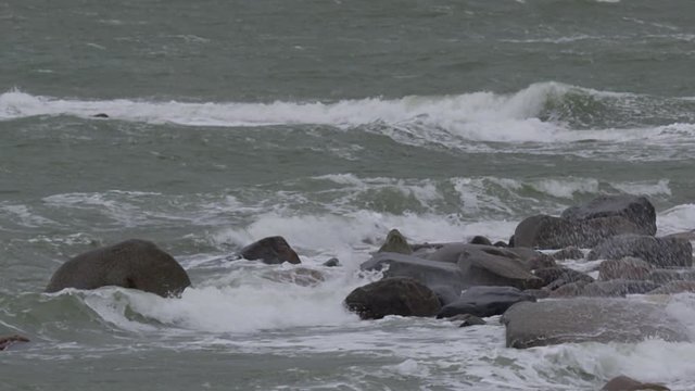 Slow motion - storm waves crash and spray against boulders