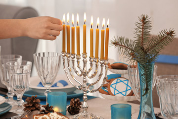 Female hand applying match to menorah on table served for Hanukkah