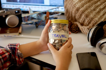 Woman holding saveing money “ travel” in a glass jar on desk work. Saving money for travel concept.