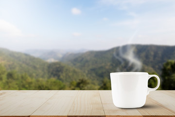 Hot coffee with steam on wooden table top on blurred mountain background
