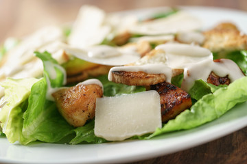 closeup shot of caesar salad with chicken on old wooden table, shallow focus