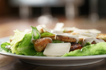 plate with fresh caesar salad with chicken on old wooden table, shallow focus