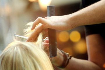 Hairdresser cutting and modeling blond hair by scissors and comb