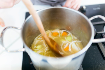 Beautiful young woman cooking soup with vegetables at home.