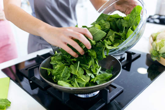 Young woman adding chard into frying pan.