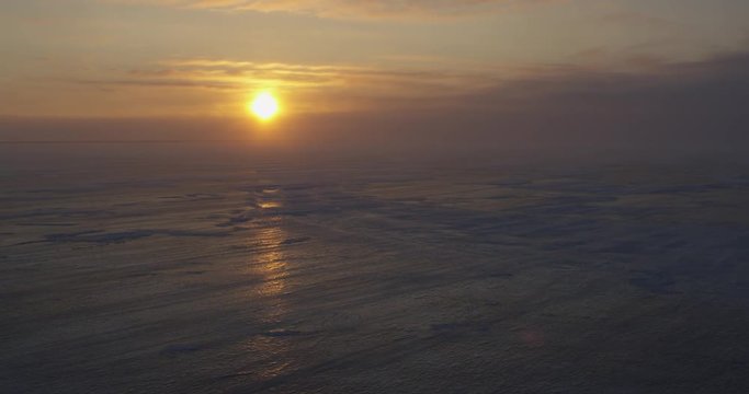Sunset on shiny sea ice as snow blows over and clouds obscure