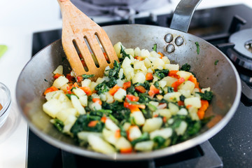 Young woman mixing chard, potatoes, red pepper and eggs into the pan.