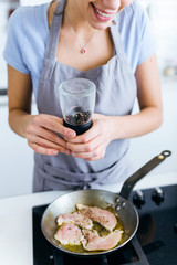 Young woman adding pepper to chicken into the pan.
