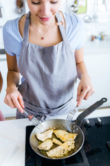 Beautiful young woman cooking chicken breast in the pan.