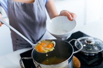Young woman serving vegetable soup in the kitchen.