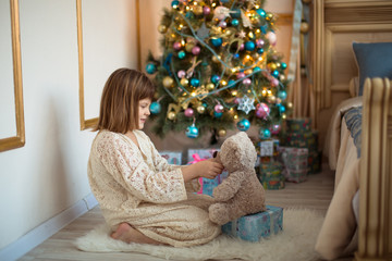 girl in lace dress plays with  bear near Christmas tree, bright