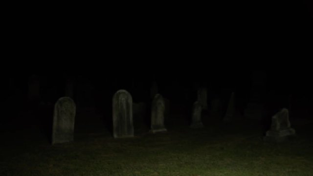 Dark pan across cemetery graveyard at night
