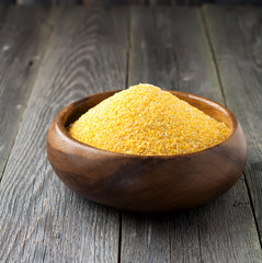 Raw corn grits polenta in a bamboo bowl on the old wooden background. Square image. Selective focus.