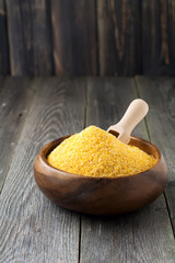 Raw corn grits polenta in a bamboo bowl on the old wooden background. Selective focus