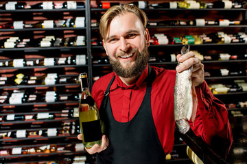 Portrait of a seller or sommelier with wine bottle and trout fish at the luxury supermarket or restaurant. Choosing wine according to the type of fish. Bottle with empty label to copy paste