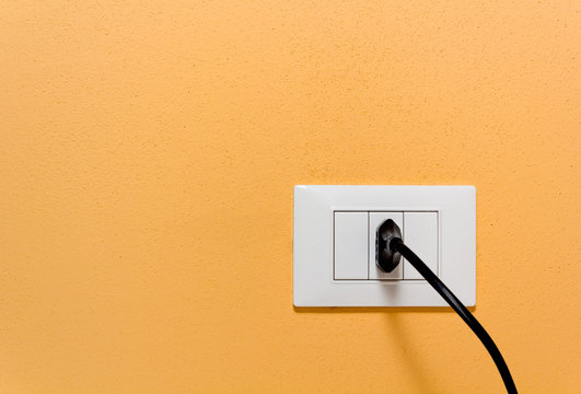 Black Plug in a Wall Socket on an Orange Wall