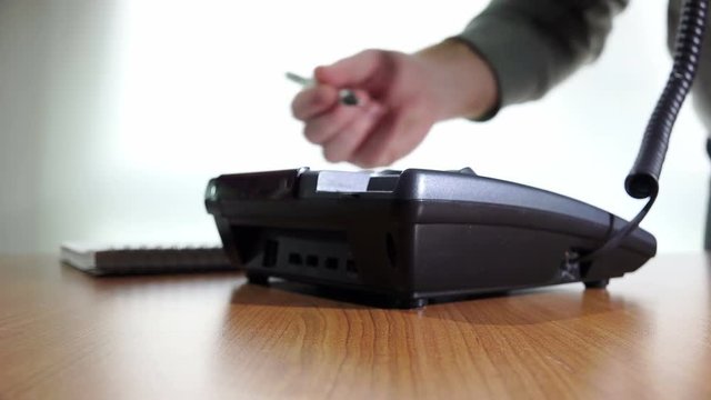 a man answers the phone and takes notes on a sheet of paper: wired, cord