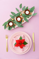 Christmas place setting in pink with golden silverware, eucalyptus and candles