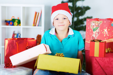 Funny boy in Santa red hat with a lot of gift boxes.