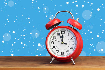 Red retro alarm clock at twelve o'clock amid flying snow.