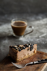 Slice of raw chocolate mousse cake with cashew, hazelnuts and dark chocolate glaze topping and coffee on a wooden and grey background. Vegan sugar, gluten free dessert. Copy space