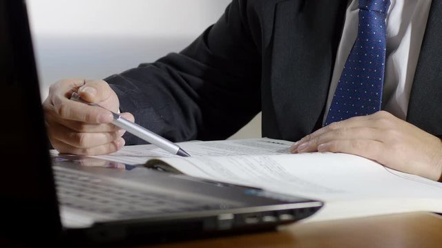 businessman at work with laptop is checking a printed list on paper sheets 