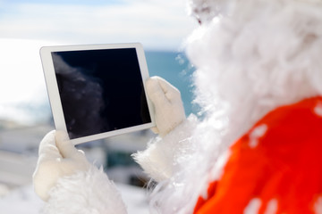 Joyful Santa holding mobile tablet computer preparing gifts Christmas background