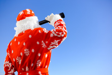 Santa Claus looking through telescope on sunny blue sky outdoors background. Closeup back side view image
