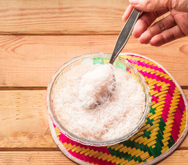Hand holding Rice in bowl and colorful tray on wooden table.