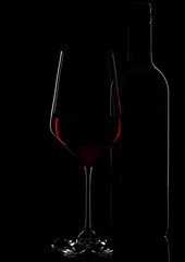 Glass of red wine with bottle close up on black