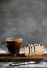 Slice of raw chocolate mousse cake with cashew, hazelnuts and dark chocolate glaze topping and coffee on a wooden and grey background. Vegan sugar, gluten free dessert. Copy space