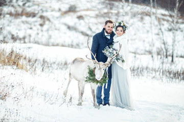 Fototapeta na wymiar Winter wedding. The bride and groom stand with a deer on a snowy meadow.