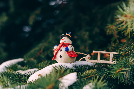 Closeup christmas decoration small snowman with red skarf and sled on the branch