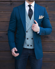 Male model in a torso jacket and a vest posing in front of a wooden wall