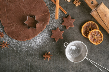 Christmas baking background dough, cookie cutters with spice, walnuts, oranges and baking accessories. Viewed from above.