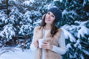 Woman holds cup of coffee with marshmallow in winter forest