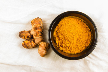 Turmeric root with bowl of powder on white cloth background