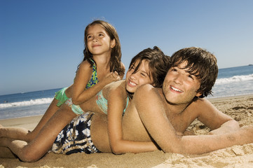 Fototapeta premium Cheerful children lying on top of each other while looking away at beach