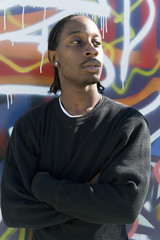 Front view of African American man with arms crossed against graffiti wall