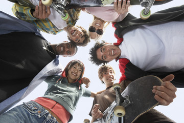 Fototapeta na wymiar Group of multiethnic friends with skateboards forming huddle against sky