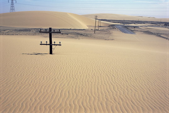 Migrating barchan sand dunes across road marked by buried telegraph poles, Kharga basin, Western Desert, Egypt