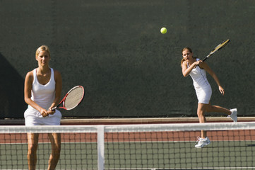 Female tennis player standing with her partner hitting shot in background