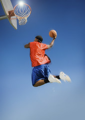 Low angle view of man dunking basketball into hoop against clear blue sky